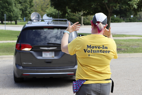 Move-in volunteer wearing a yellow shirt directs a car during residence hall move-in on campus.