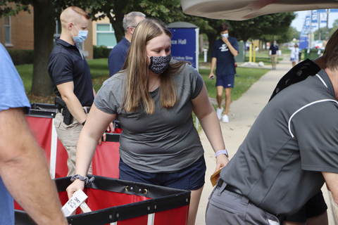 Student volunteer wearing a mask pushes a red move-in cart while assisting with residence hall move-in.
