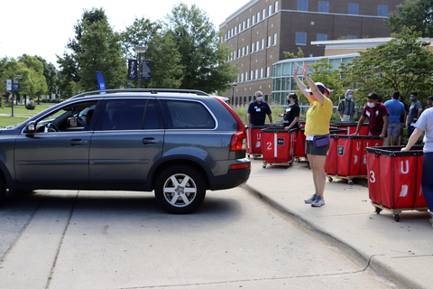 Volunteers guide a car past red move-in carts lined along a campus sidewalk during move-in day.