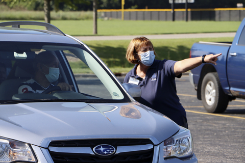 Staff member wearing a mask points to direct a car during campus residence hall move-in.